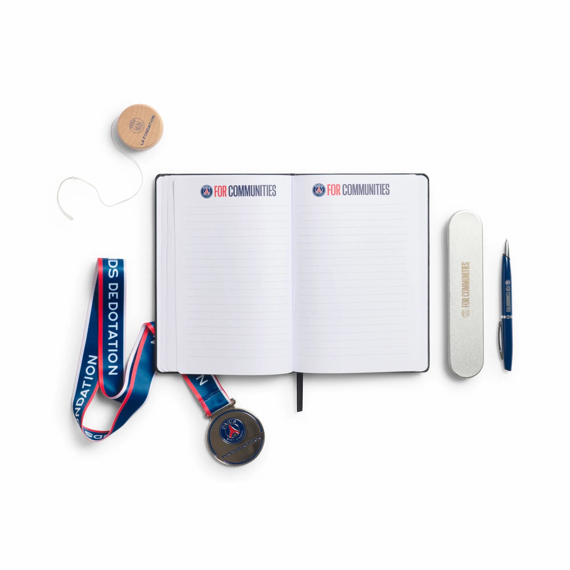 PSG For Communities Flatlay mit aufgeschlagenem Notizbuch, Medaille mit Lanyard, Holz-Yo-Yo und Kugelschreiber im Etui – La Fondation Paris Saint-Germain