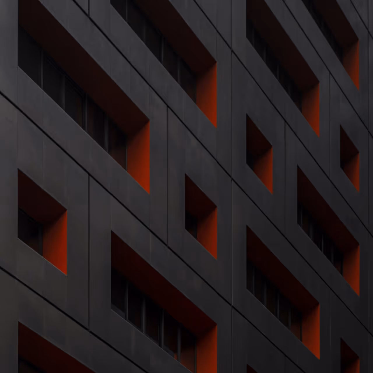 Modern building facade with dark gray geometric patterns and deep orange recessed window frames.