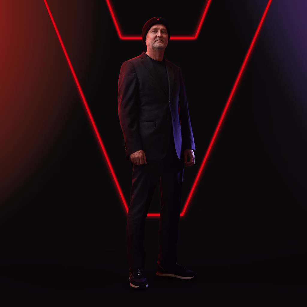 Middle-aged man with light beard wearing a black beanie and dark blazer against a red and purple gradient background.