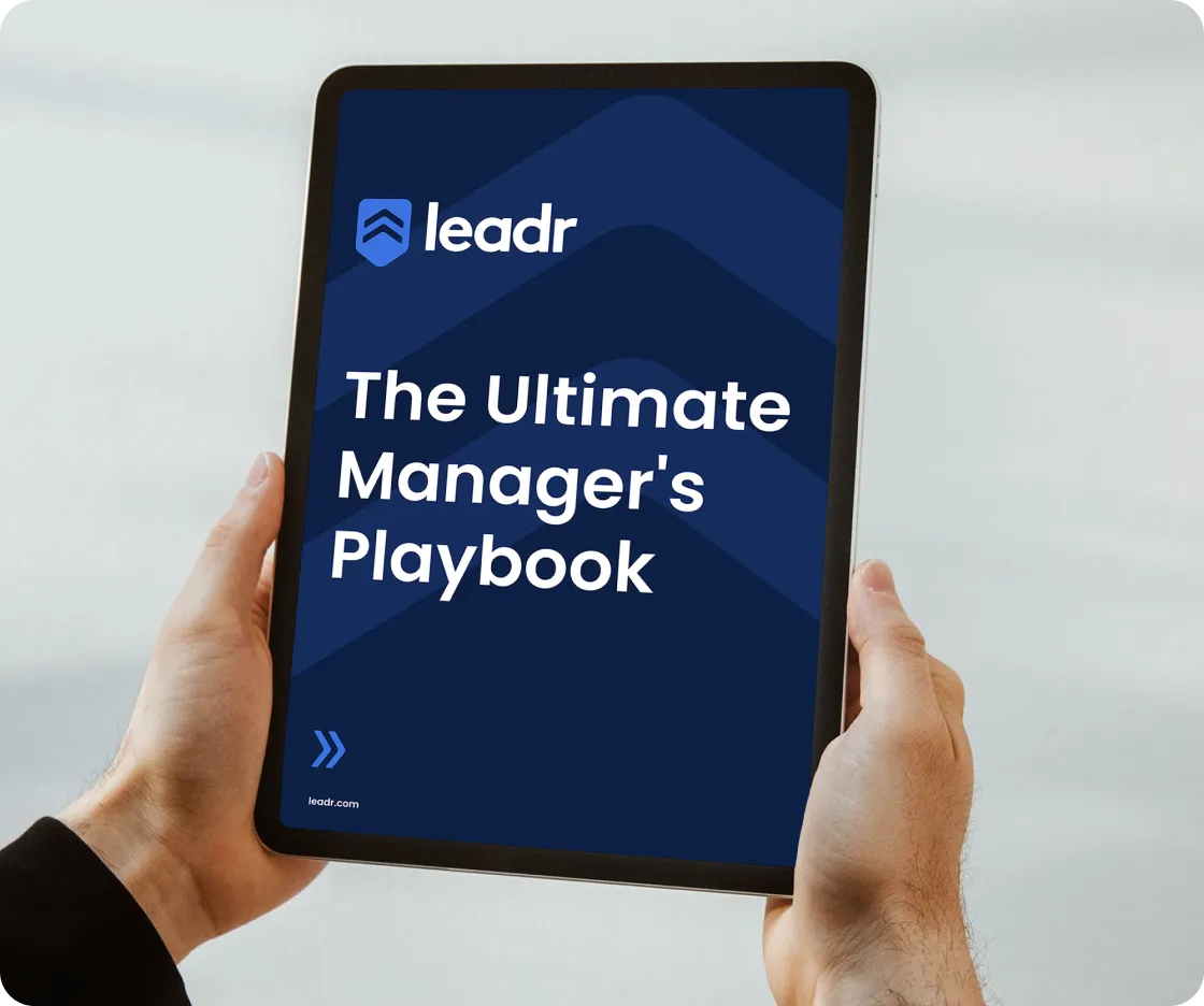 ablet screen showing Leadr branding and "The Ultimate Manager's Playbook" text, held by two hands
