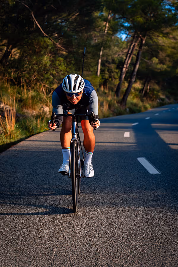 Cyclist wearing a helmet and sunglasses rides a bike fast on a sunlit forest road.