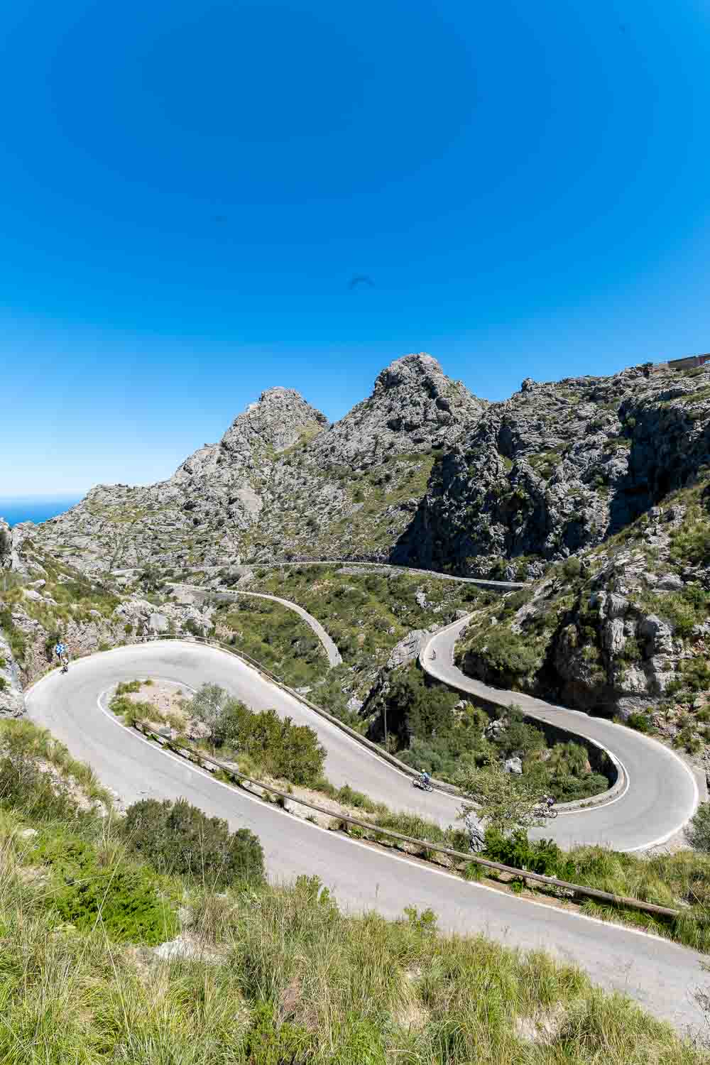 Curvy mountain road winding sharply through rocky hills under a bright blue sky.