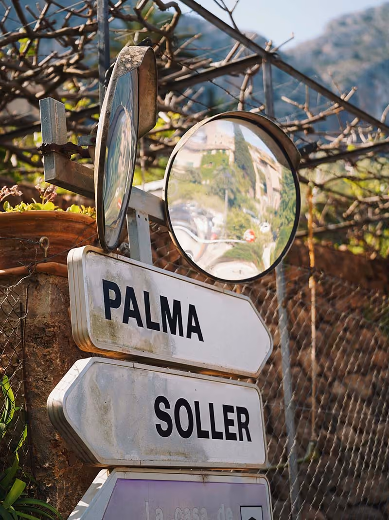 Road signs pointing to Palma and Soller with two convex mirrors mounted above them.