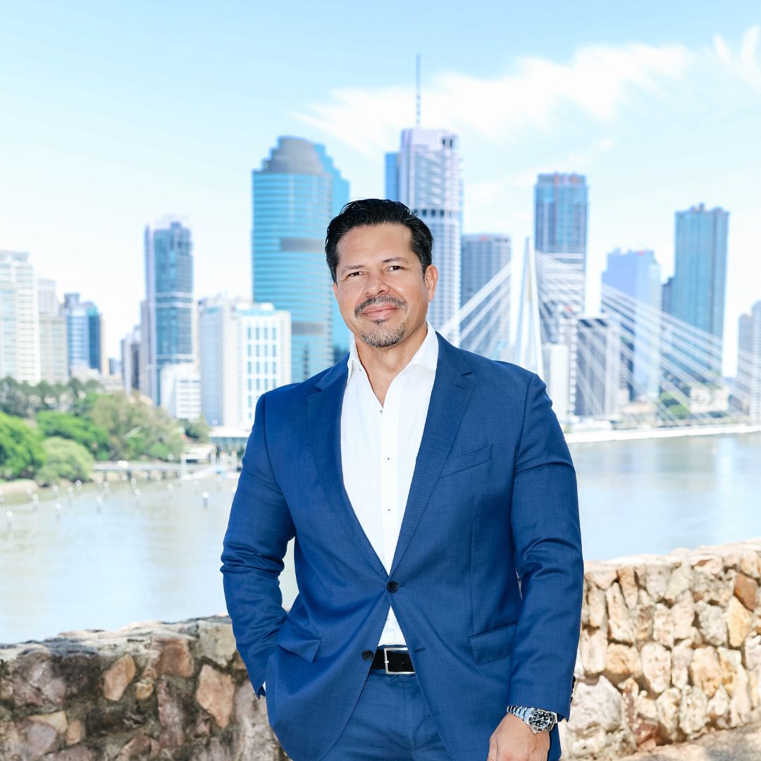 Paul Rojas in a blue suit and white shirt standing with hands in pockets in a dimly lit indoor space.