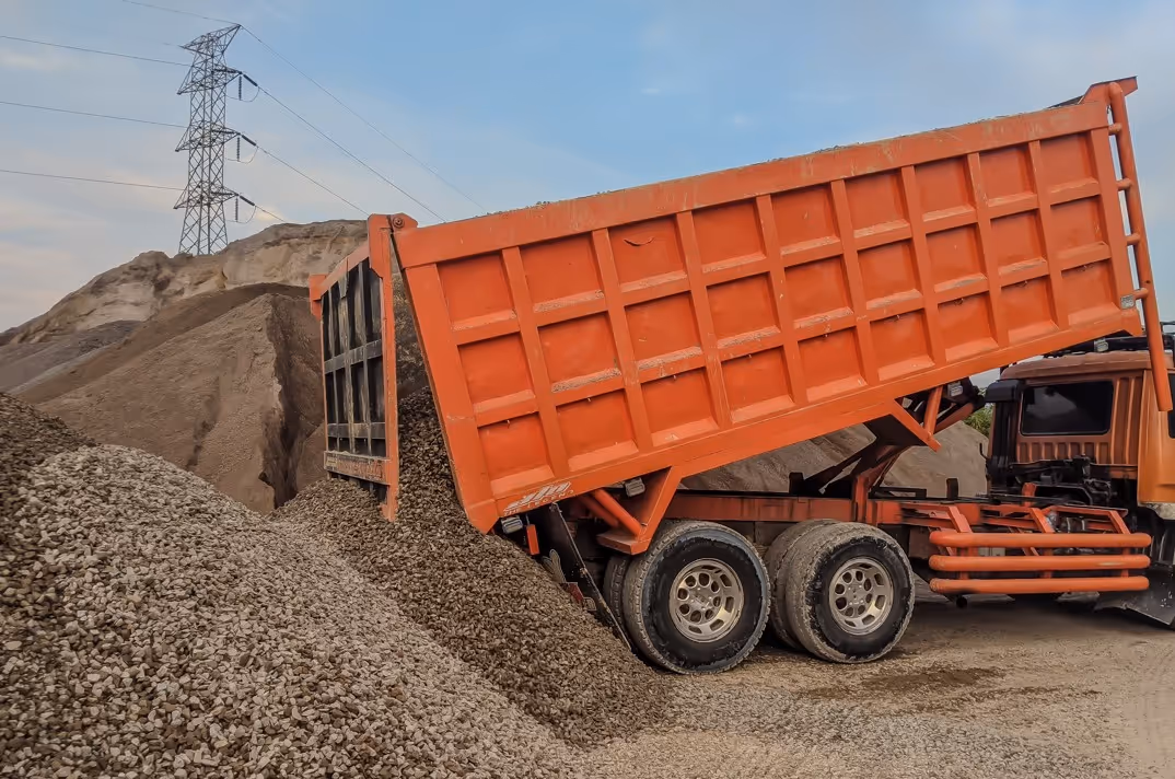 Orange dump truck unloading gravel at construction site for aggregate hauling and material delivery services