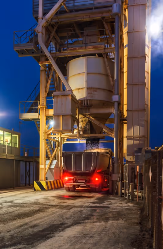 Dump truck loading coal at industrial facility at night for bulk material hauling and transportation services