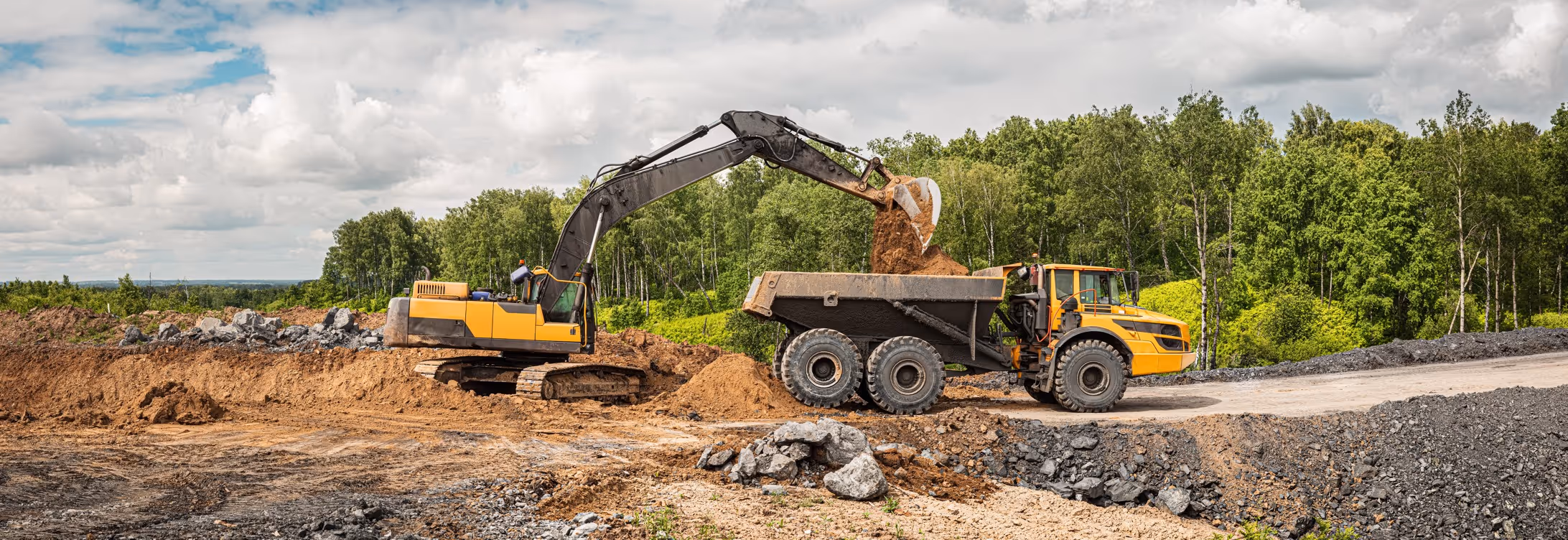 Yellow excavator loading dirt into articulated dump truck at construction site for earthwork and hauling services