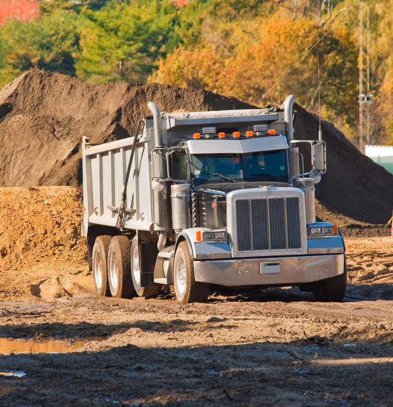 Gray dump truck at construction site with dirt piles providing heavy hauling and earthwork transportation services