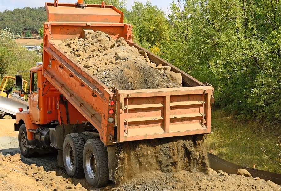 Orange dump truck unloading gravel and stone for commercial and construction hauling transportation services