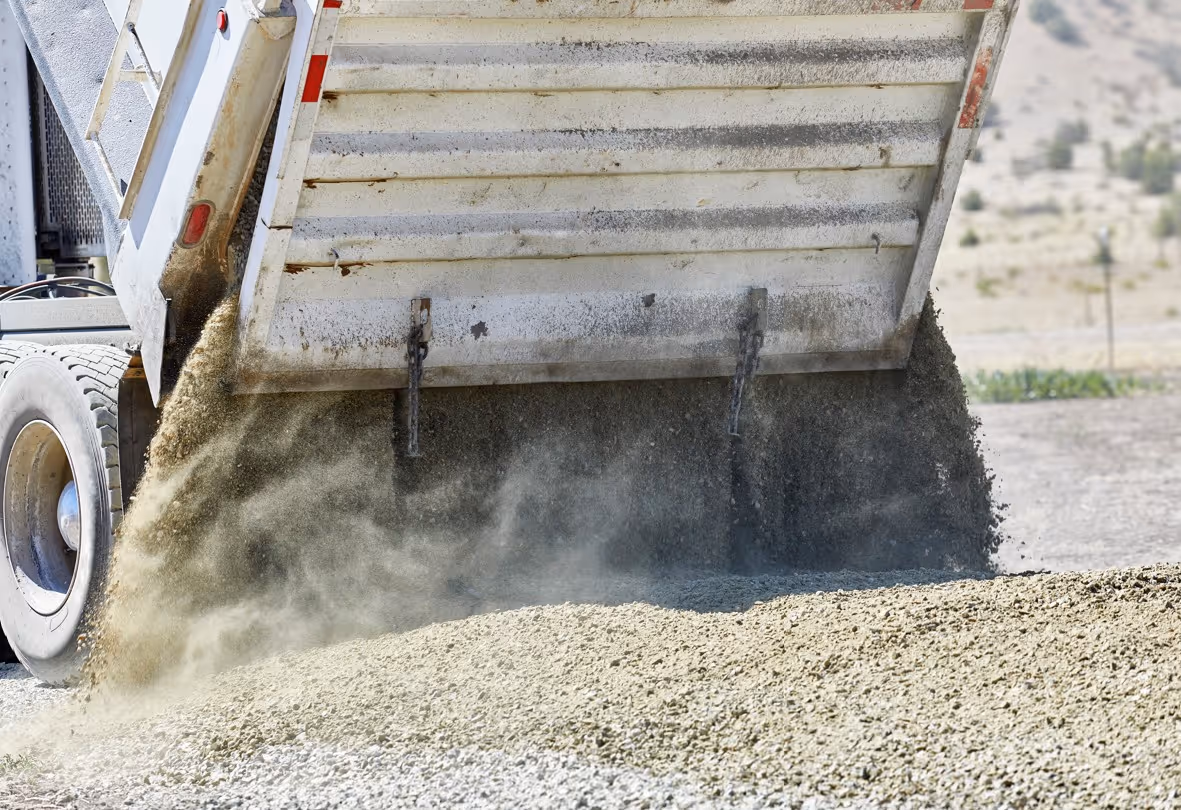 Dump truck unloading gravel with raised bed dumping aggregate material at construction site
