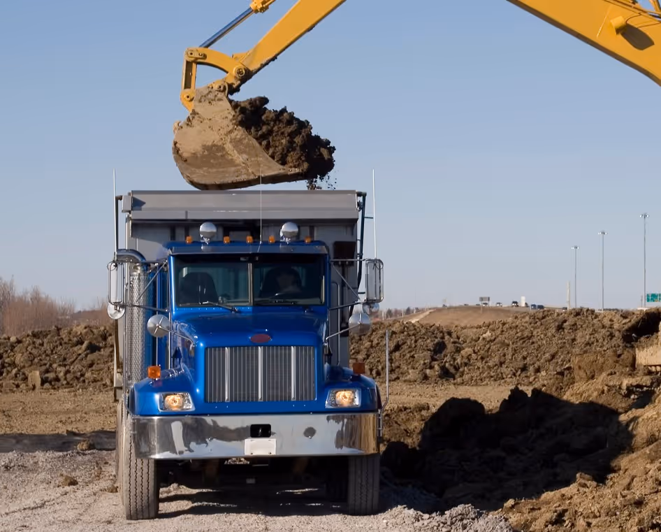 Excavator loading commercial dump truck with soil for bulk dirt transport and hauling services