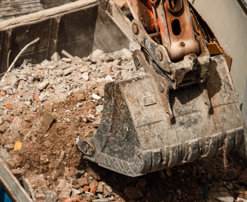 Excavator bucket filled with concrete and brick demolition debris for commercial C&D waste removal