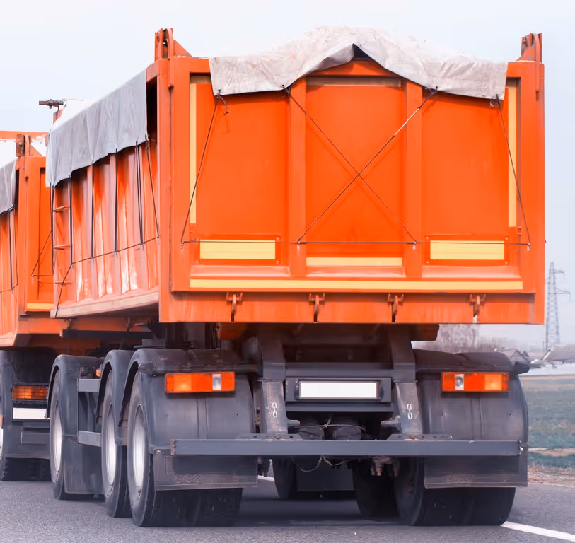Orange dump truck with tarp cover for commercial dry bulk material transport services