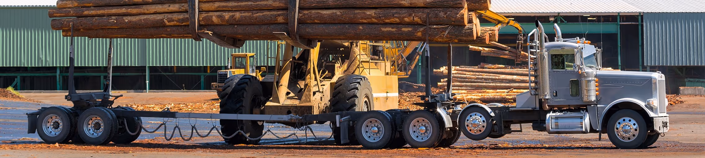 Log loader on flatbed trailer carrying timber for commercial forestry product transport services