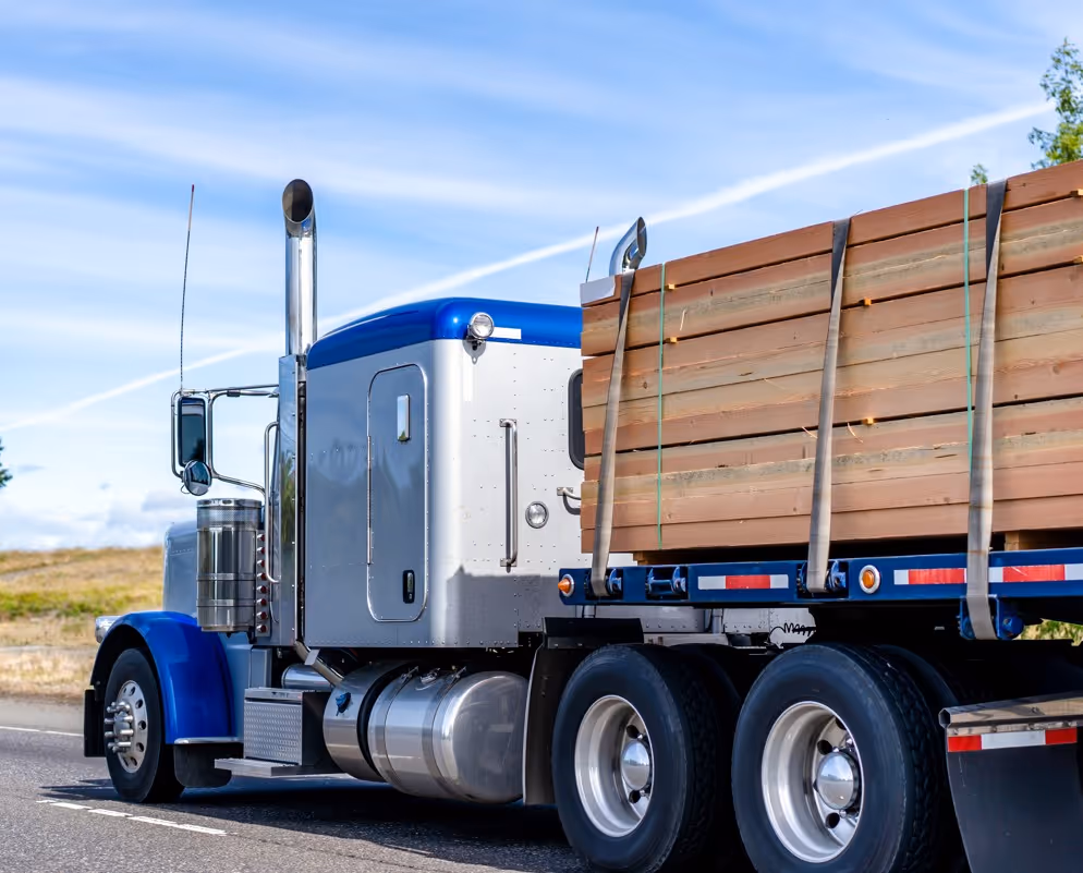 Blue semi truck hauling stacked lumber bundles for commercial forest product transport services