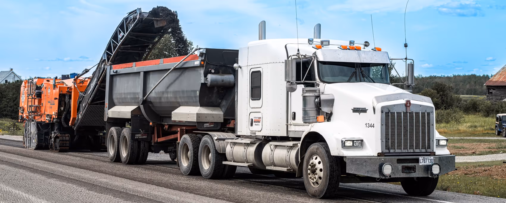 White semi truck hauling paving milling machine on lowboy trailer for road maintenance equipment transport