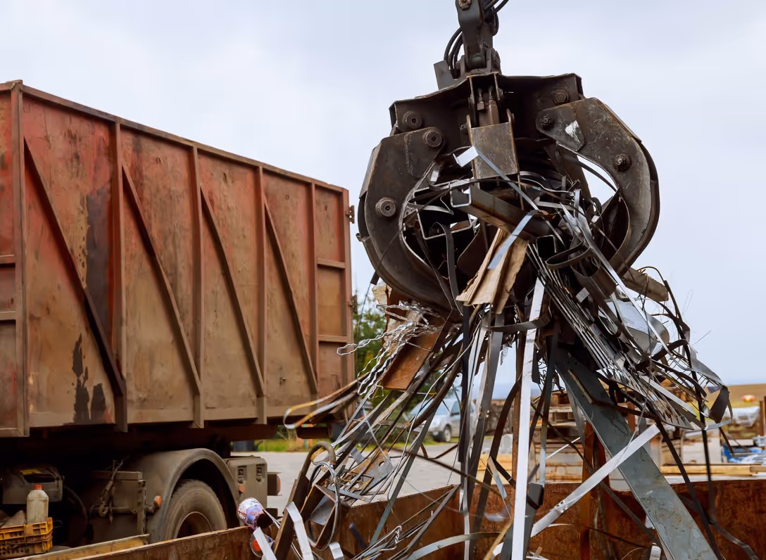 Grapple claw lifting scrap metal over container for commercial metal recycling hauling services