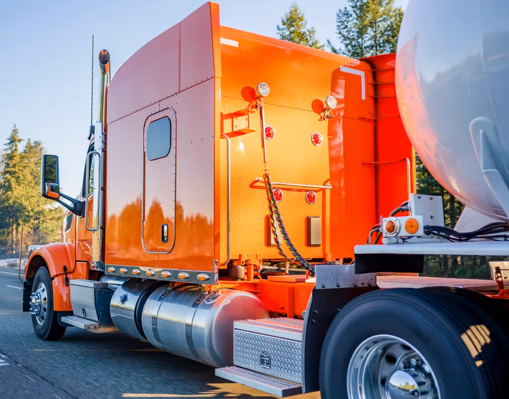 Orange commercial truck pulling stainless steel tank trailer for bulk liquid transport services