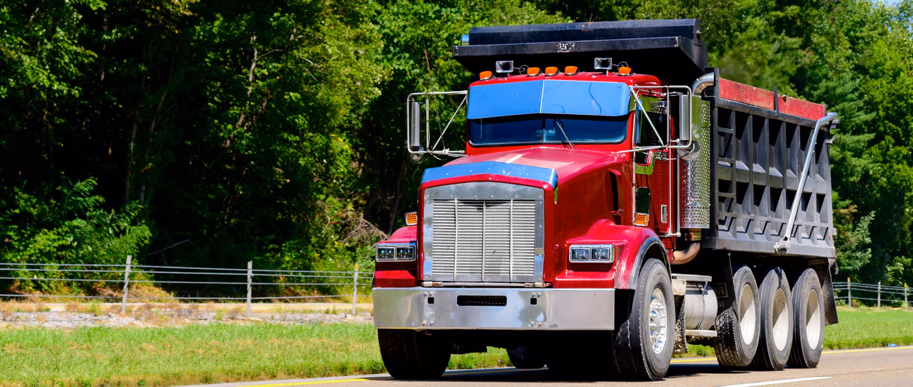 Red tri-axle dump truck for heavy-duty construction material hauling and commercial transportation services