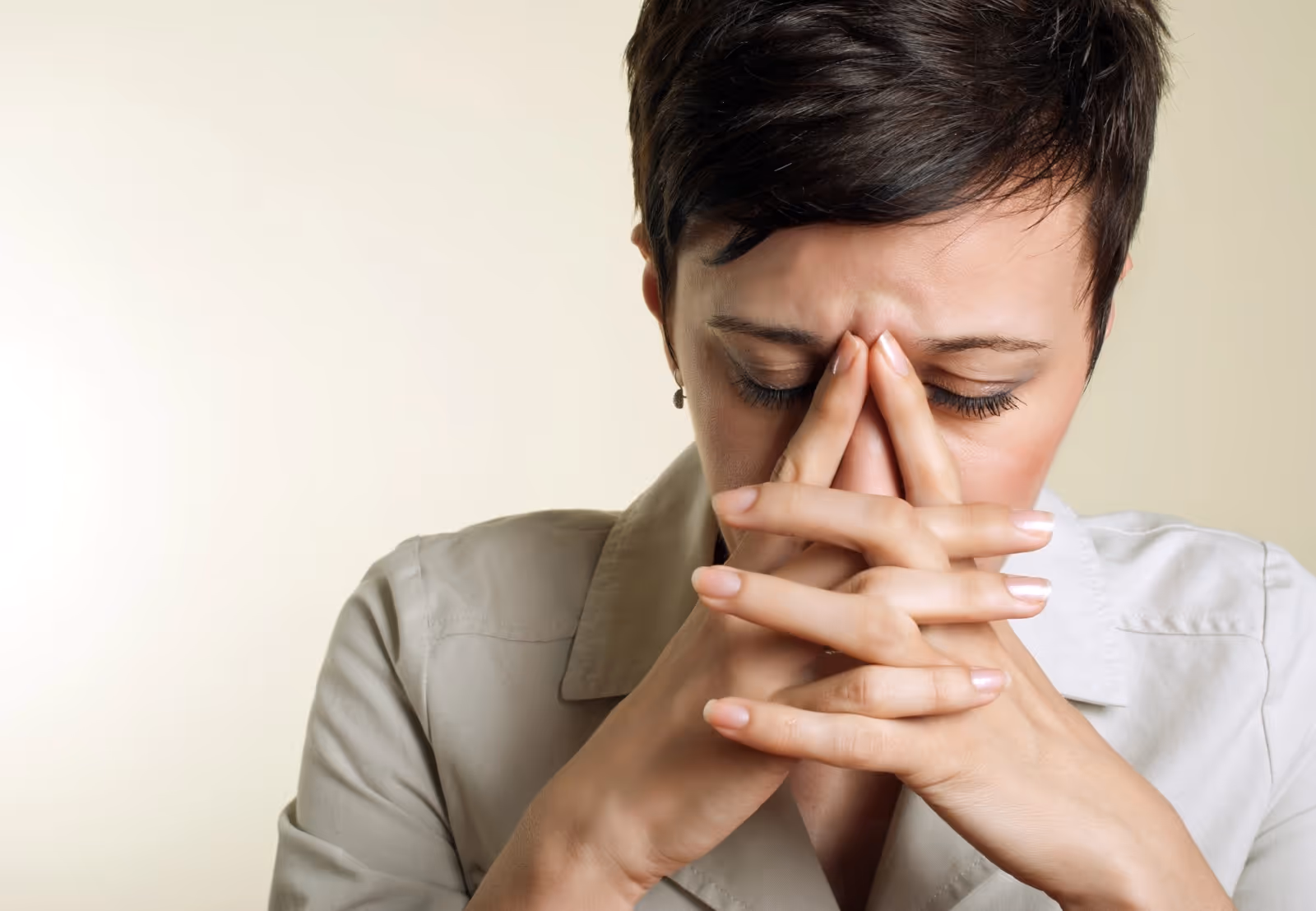 Woman with short dark hair pressing fingers against her nose and eyes closed, appearing stressed or in pain.