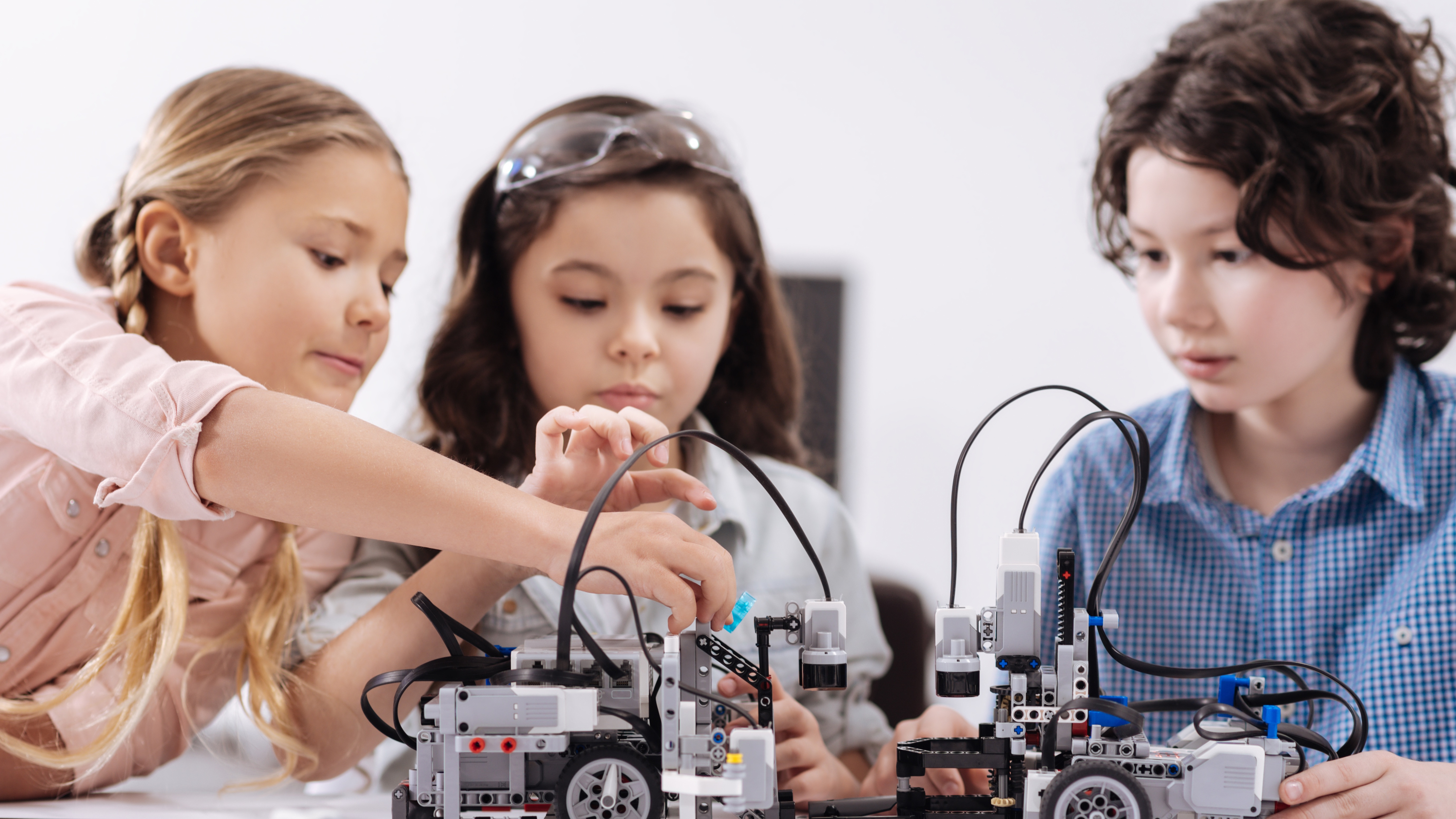 Three children working together assembling robotic vehicles with wires and sensors.