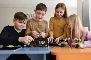 Four children working together on assembling small robotics projects at a table.