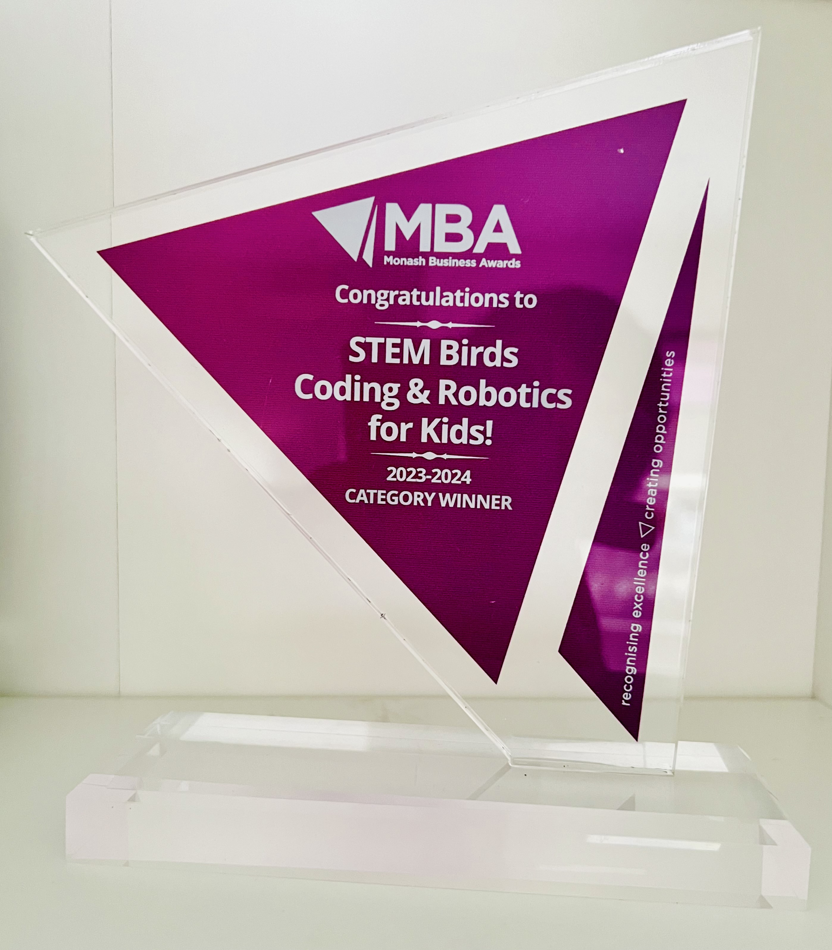 Transparent triangular award with purple insert reading 'MBA Monash Business Awards Congratulations to STEM Birds Coding & Robotics for Kids! 2023-2024 Category Winner'.