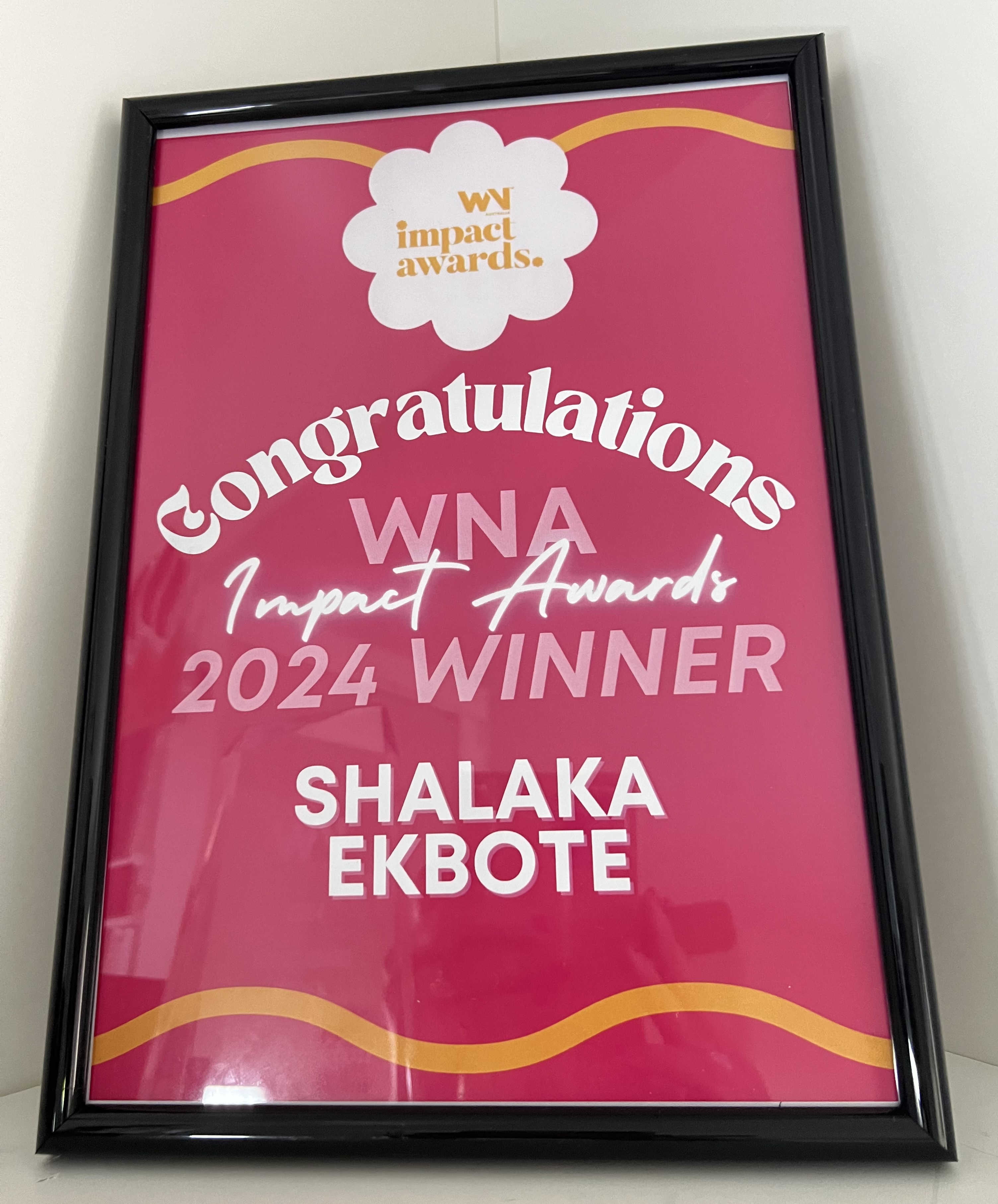 Framed pink poster congratulating Shalaka Ekbote as the 2024 WNA Impact Awards winner.
