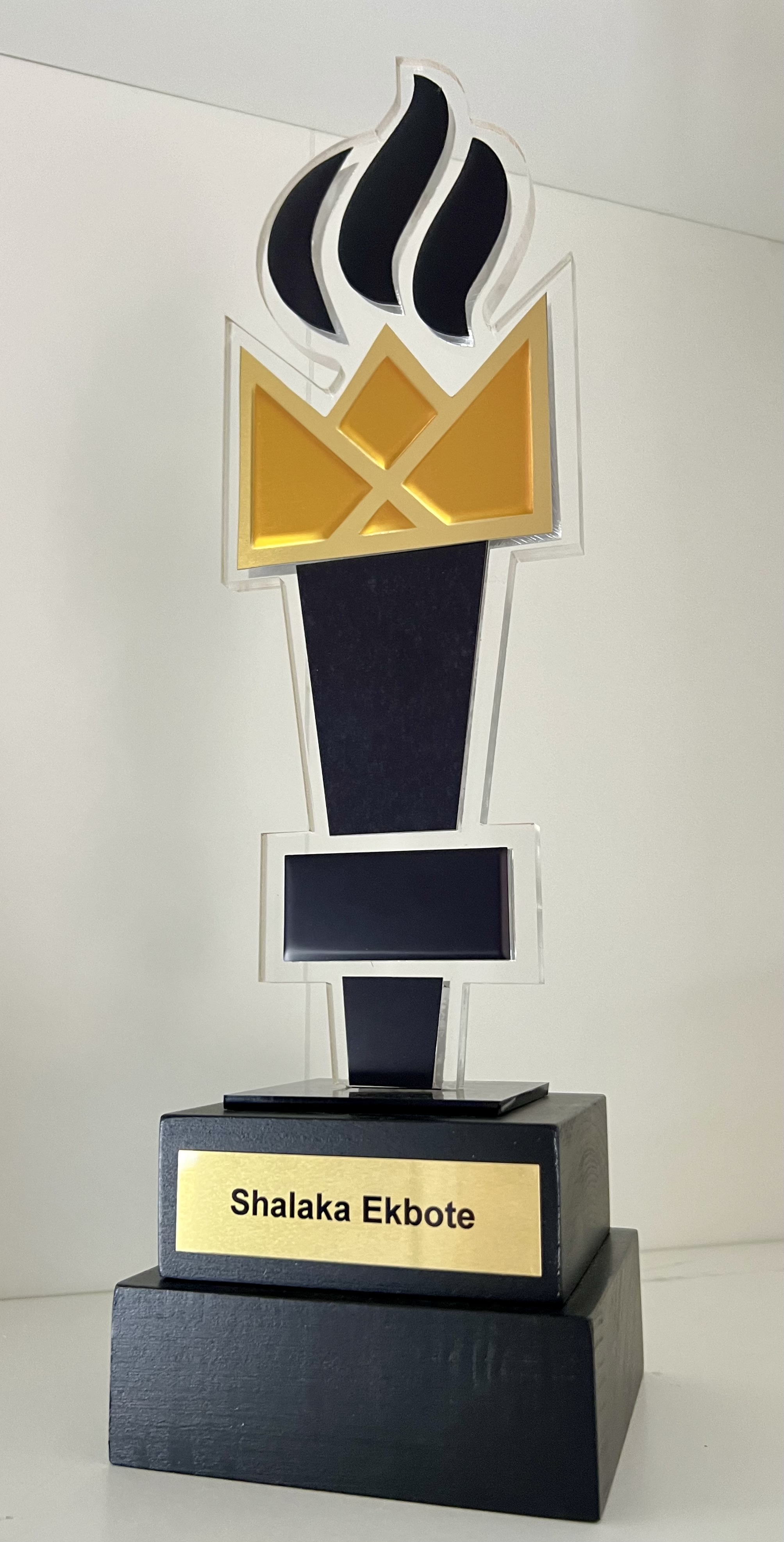 Black and gold trophy with a flame design on top and a nameplate reading Shalaka Ekbote.