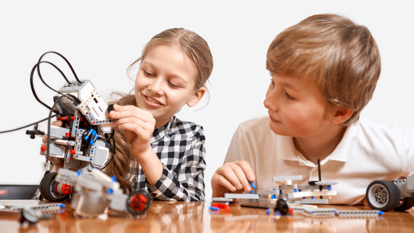 Two children building and examining robots with electronic and mechanical parts on a wooden table.