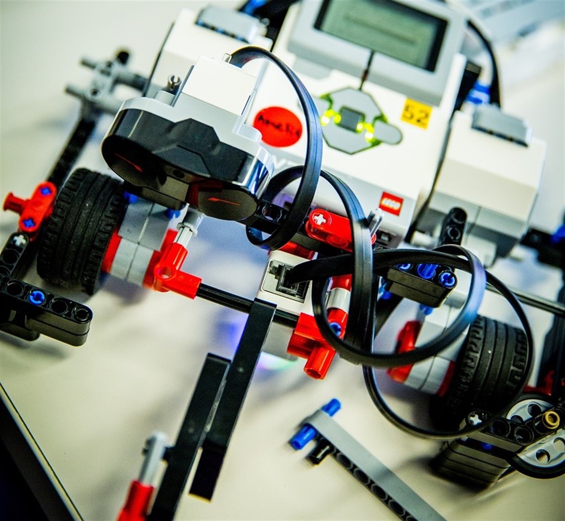 Close-up of a LEGO Mindstorms robot with sensors, wheels, and connected cables on a white surface.
