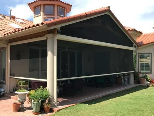 Enclosed patio with retractable screen on a suburban house, surrounded by plants and green lawn.