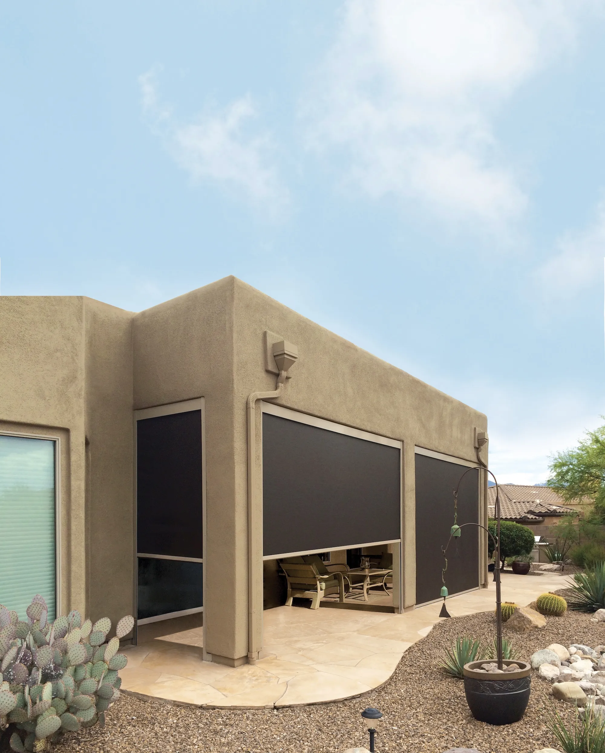 Desert-style patio with retractable black outdoor shades partially lowered on a stucco house.