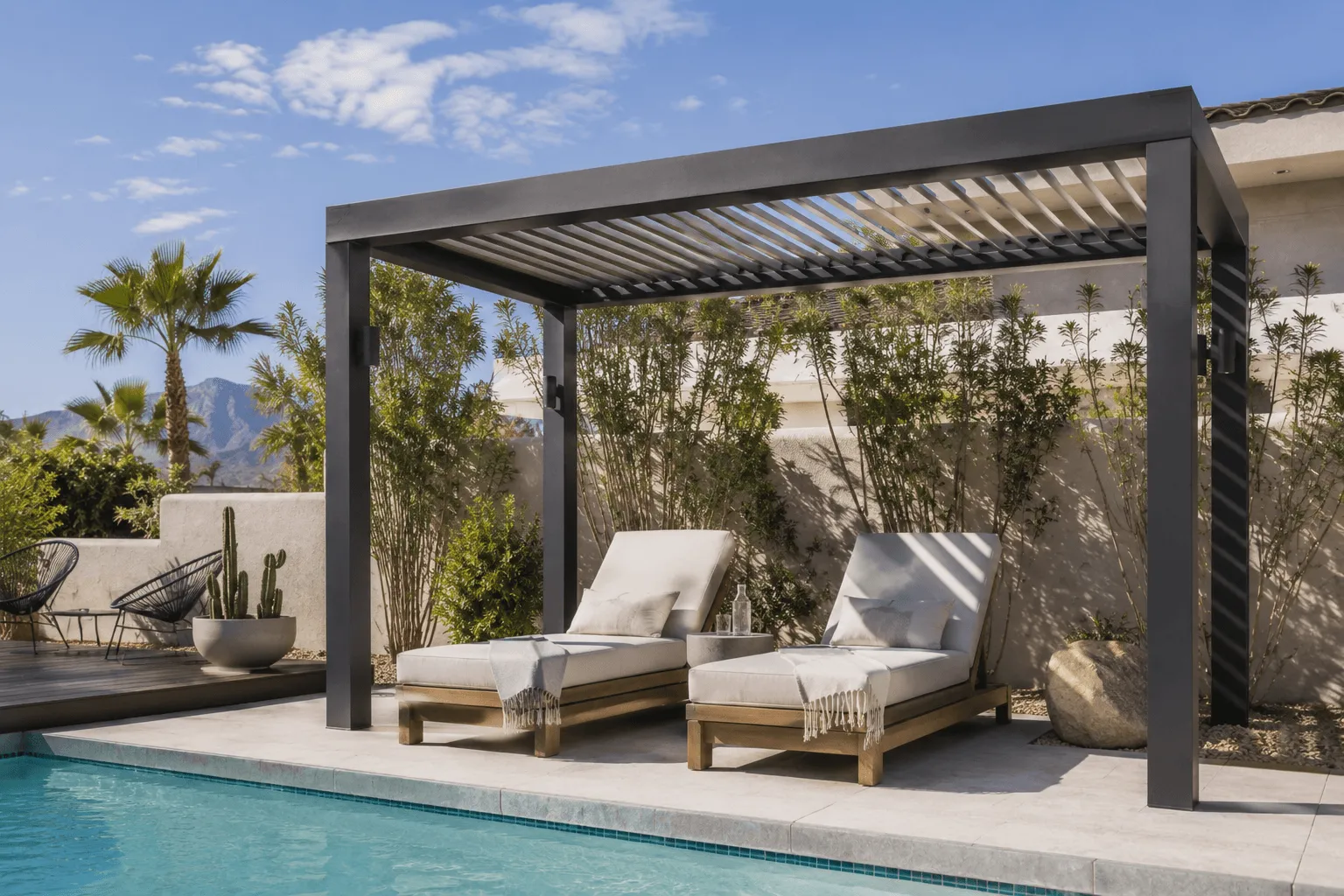 Louvered pergola shading two poolside lounge chairs with desert plants and mountain views