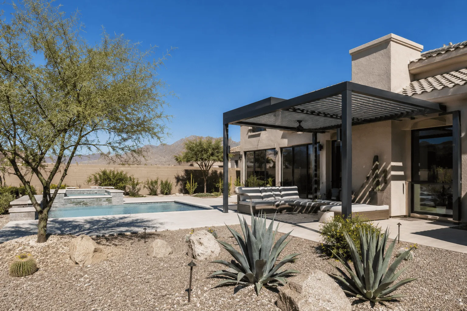 Attached louvered pergola shading a patio beside a pool, with desert landscaping and mountain views