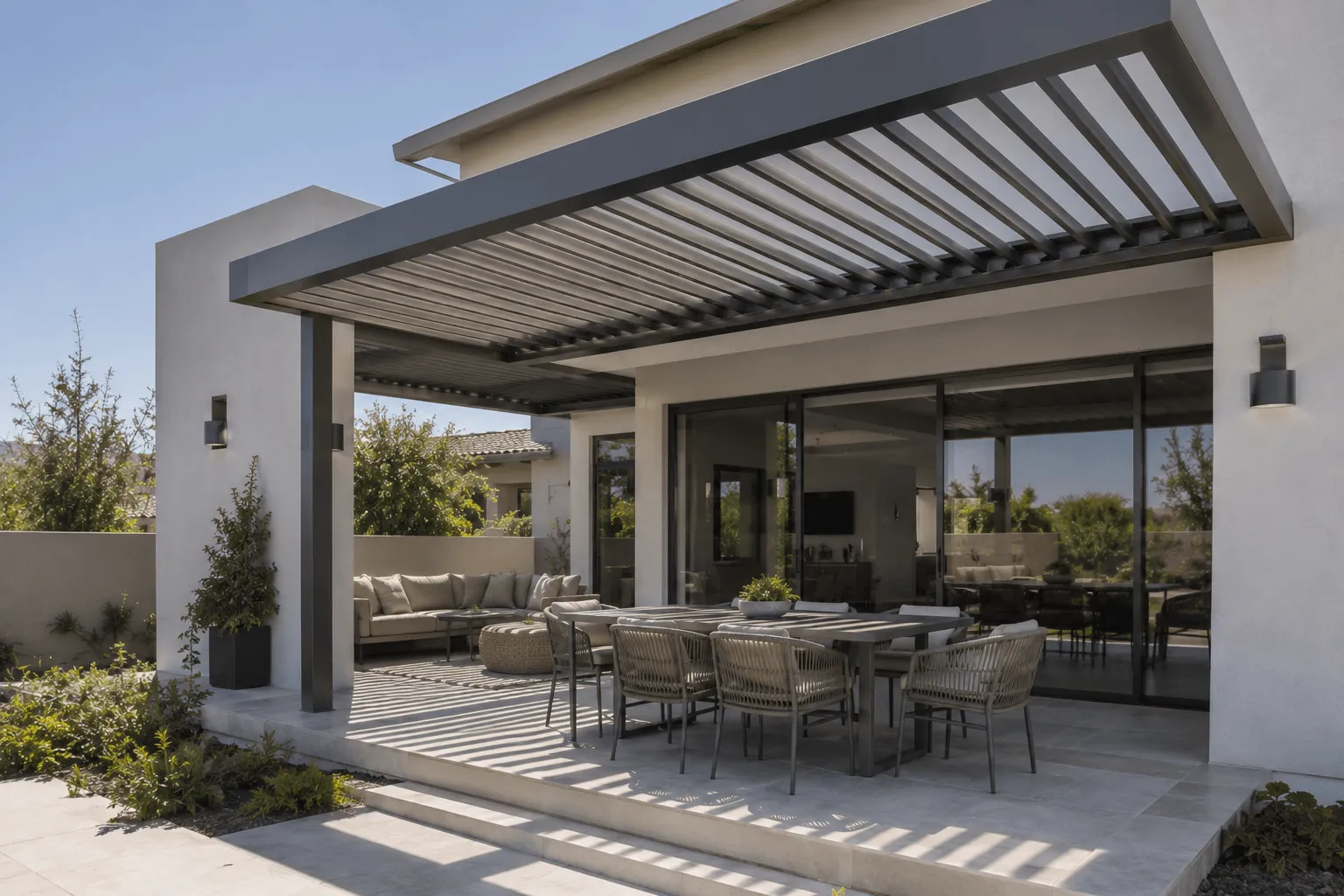 Louvered pergola attached to a modern home, shading an outdoor dining table next to sliding glass doors