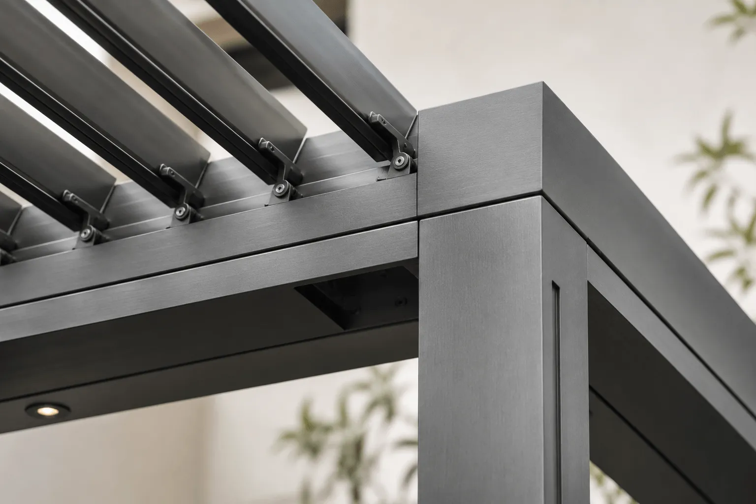 Close-up of an aluminum pergola corner joint showing the louvered roof slats and brushed metal finish