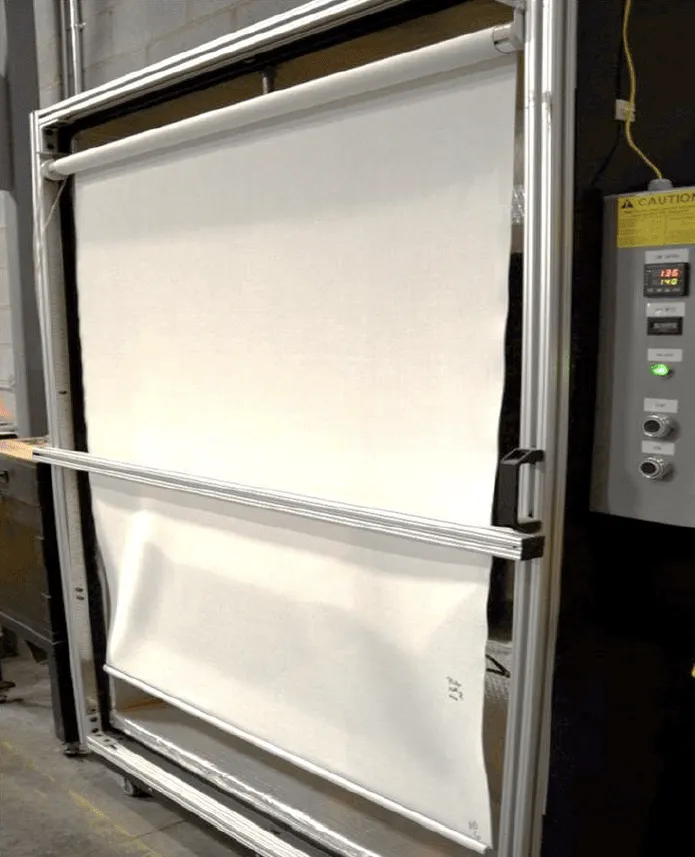 Machine holding a large rolled fabric sheet stretched vertically inside a metal frame, next to a control panel with display and buttons on a factory floor.
