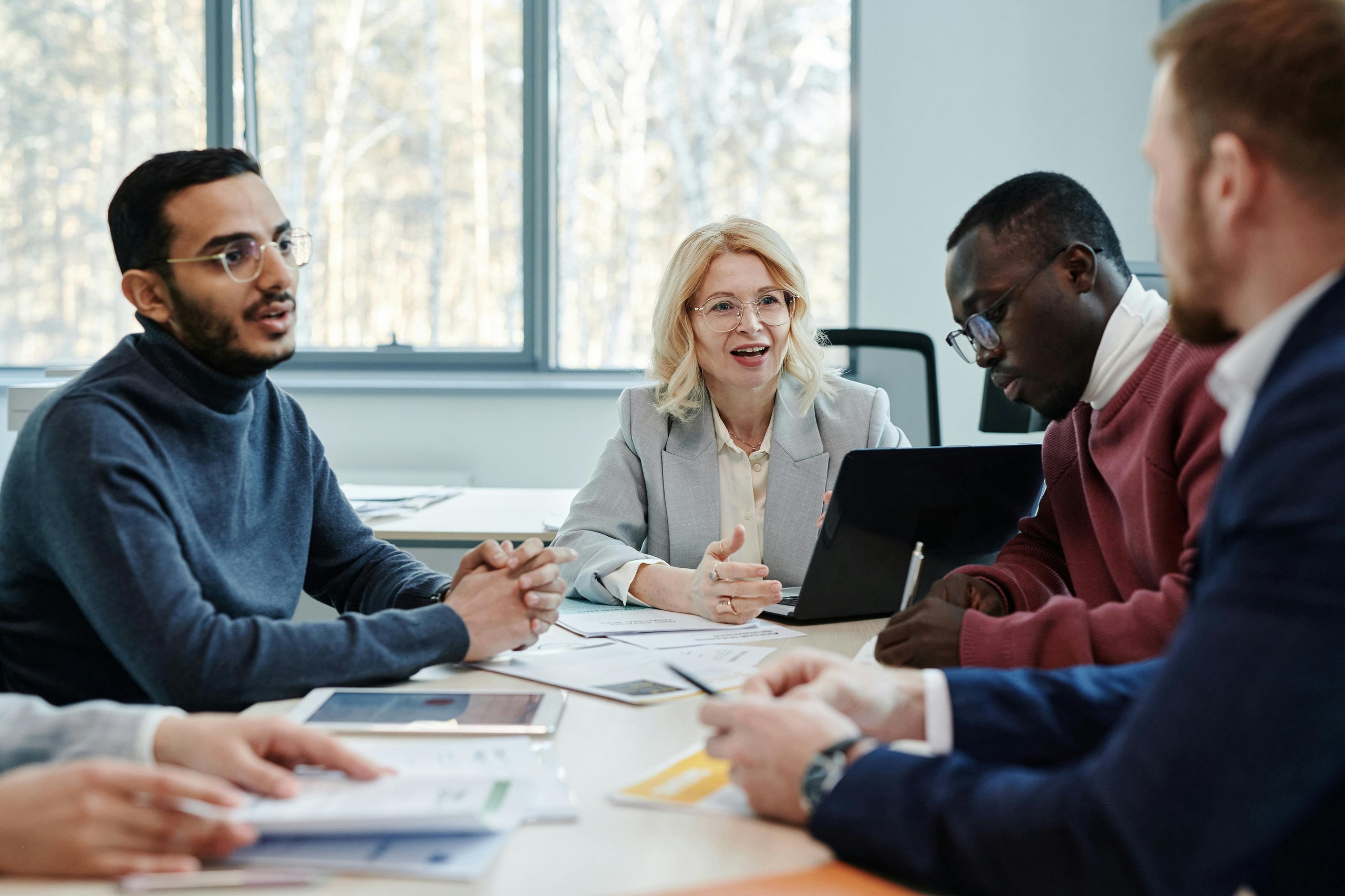 Diverse group of four people having a business meeting around a table with documents and laptops in a bright office.
