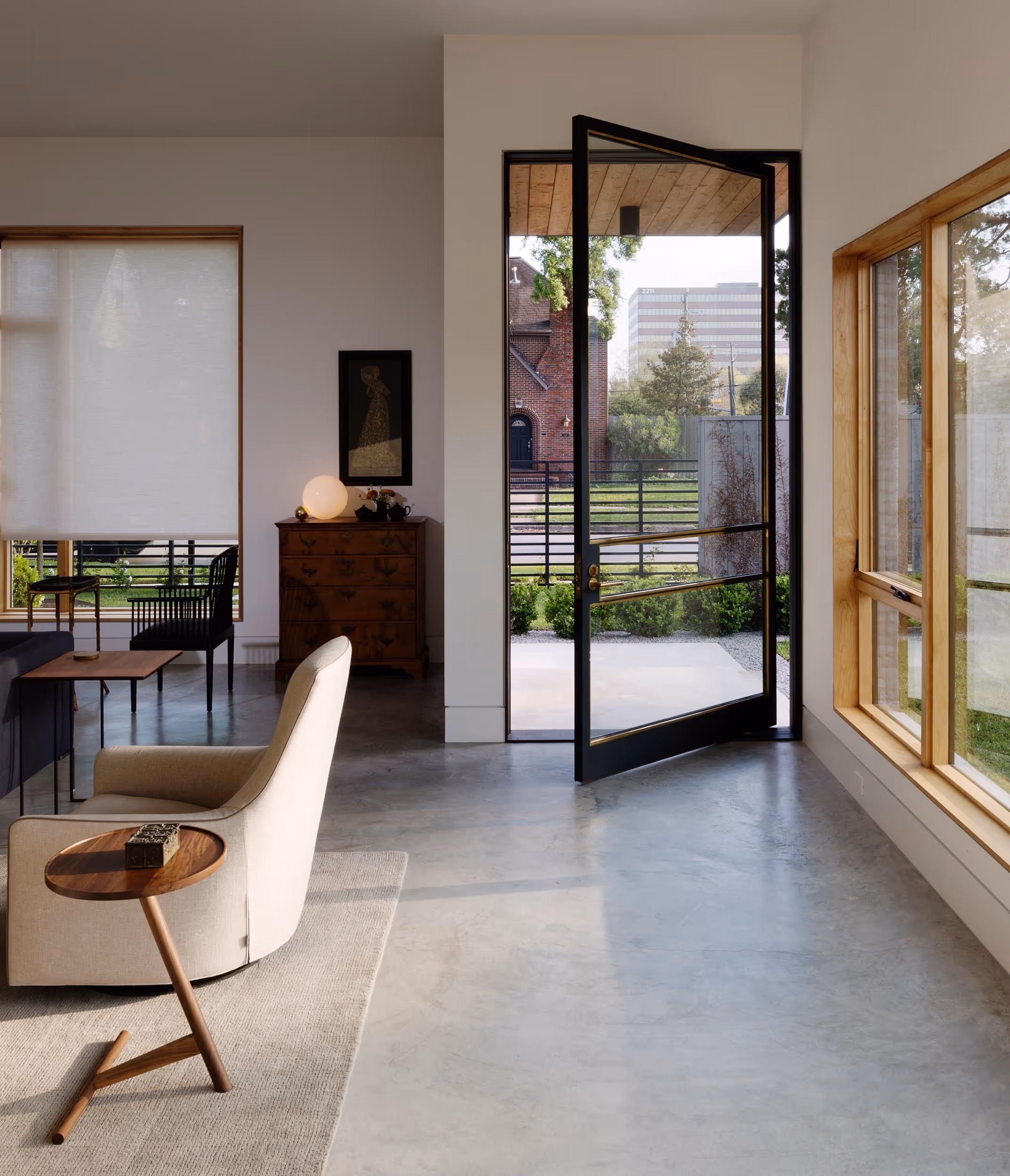 View of living room with white chair and wood table at the left and a large black rimmed glass door ajar leading to the outdoor space