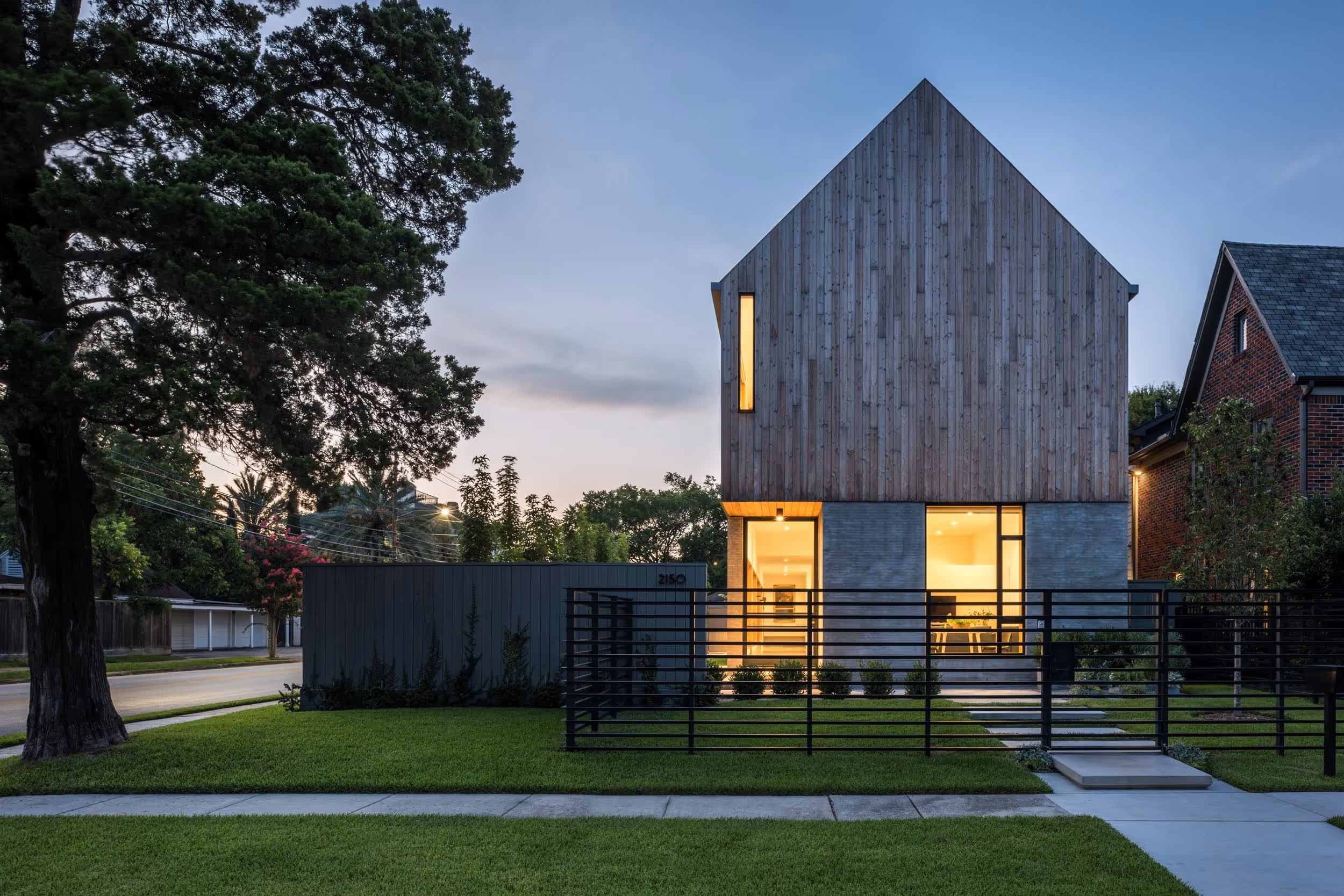 Exterior view of wood paneled home on a corner lot during the evening, with windows emitting a yellow glow