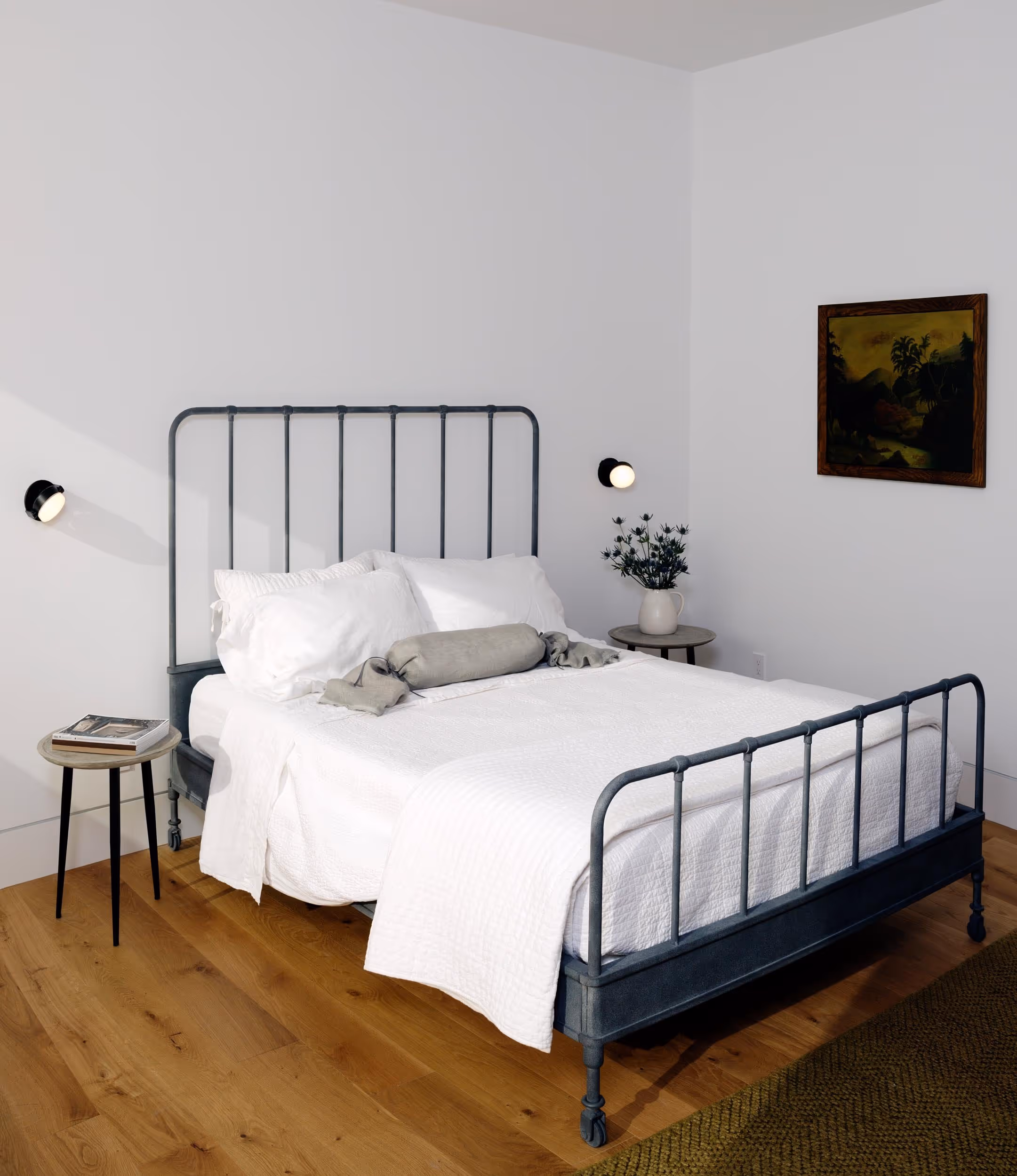 White bedroom with iron bed frame, white bedding, and sconces on either side of the bed