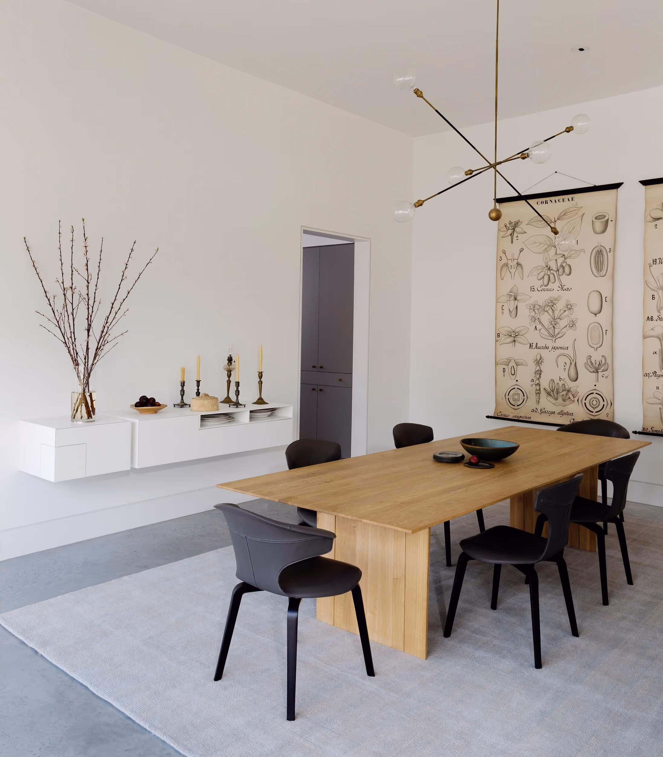 Dining room with long wood table and black chairs, white floating shelf with decor on the wall