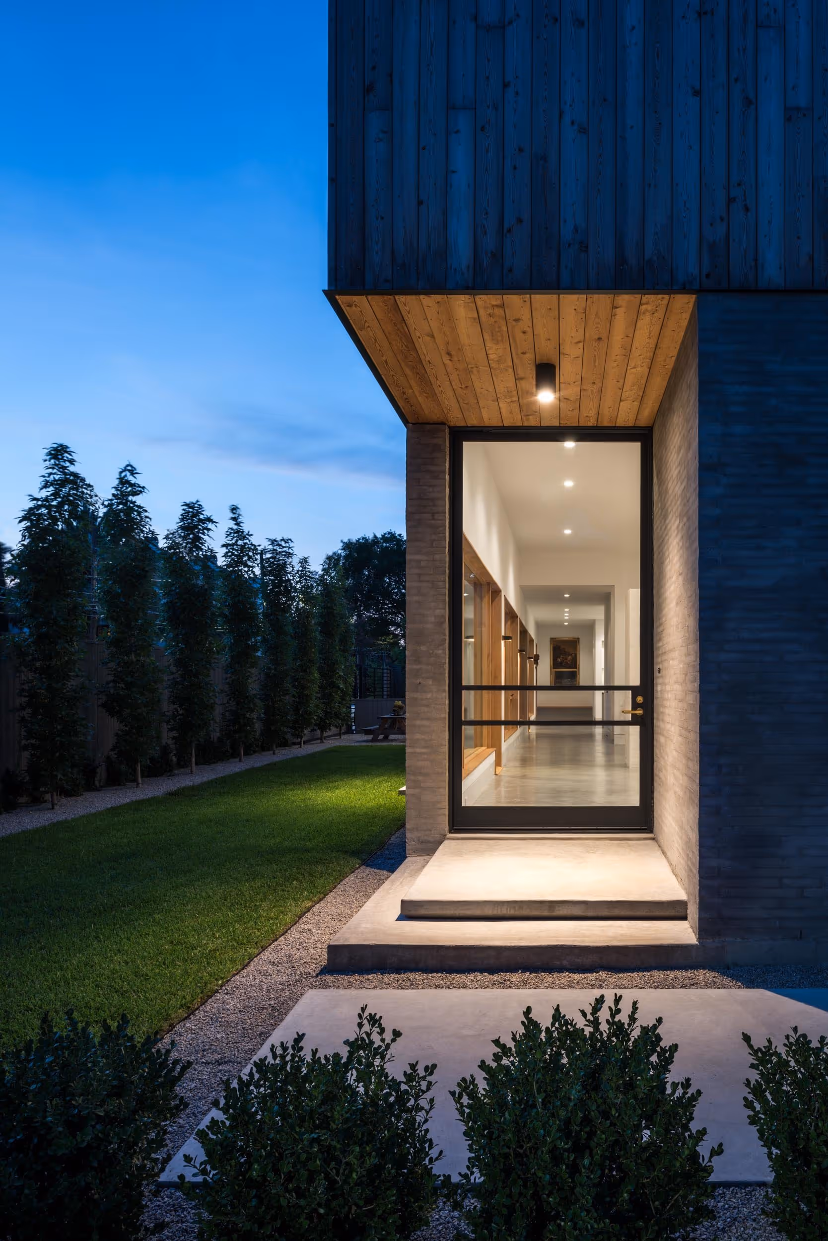 Exterior view of entrance to wood paneled home in the evening with overhead light illuminating the porch