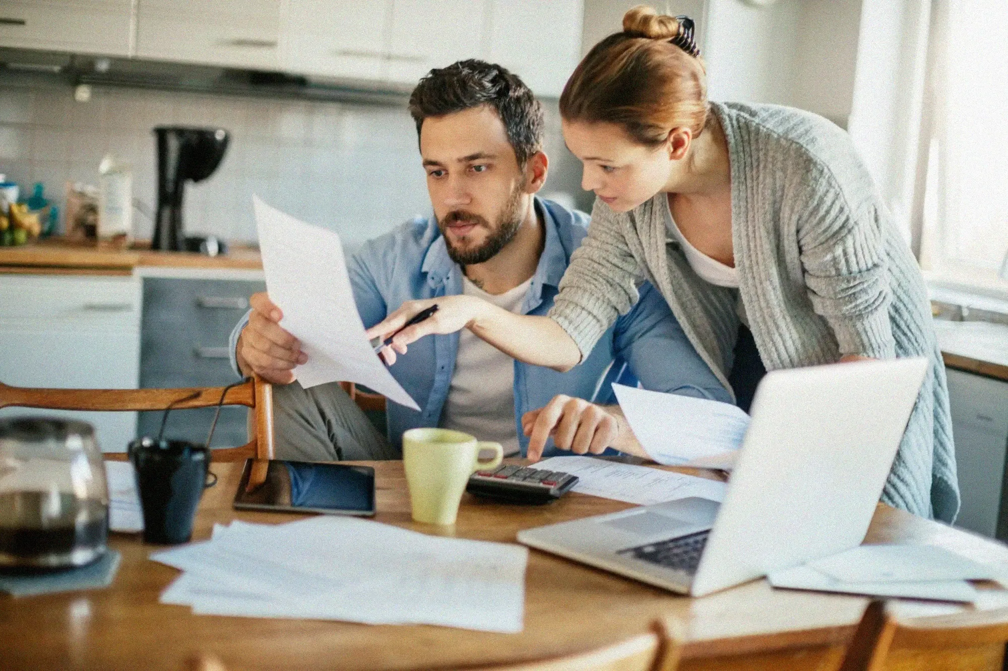 Couple reviewing financial documents together at a kitchen table with a laptop and calculator.
