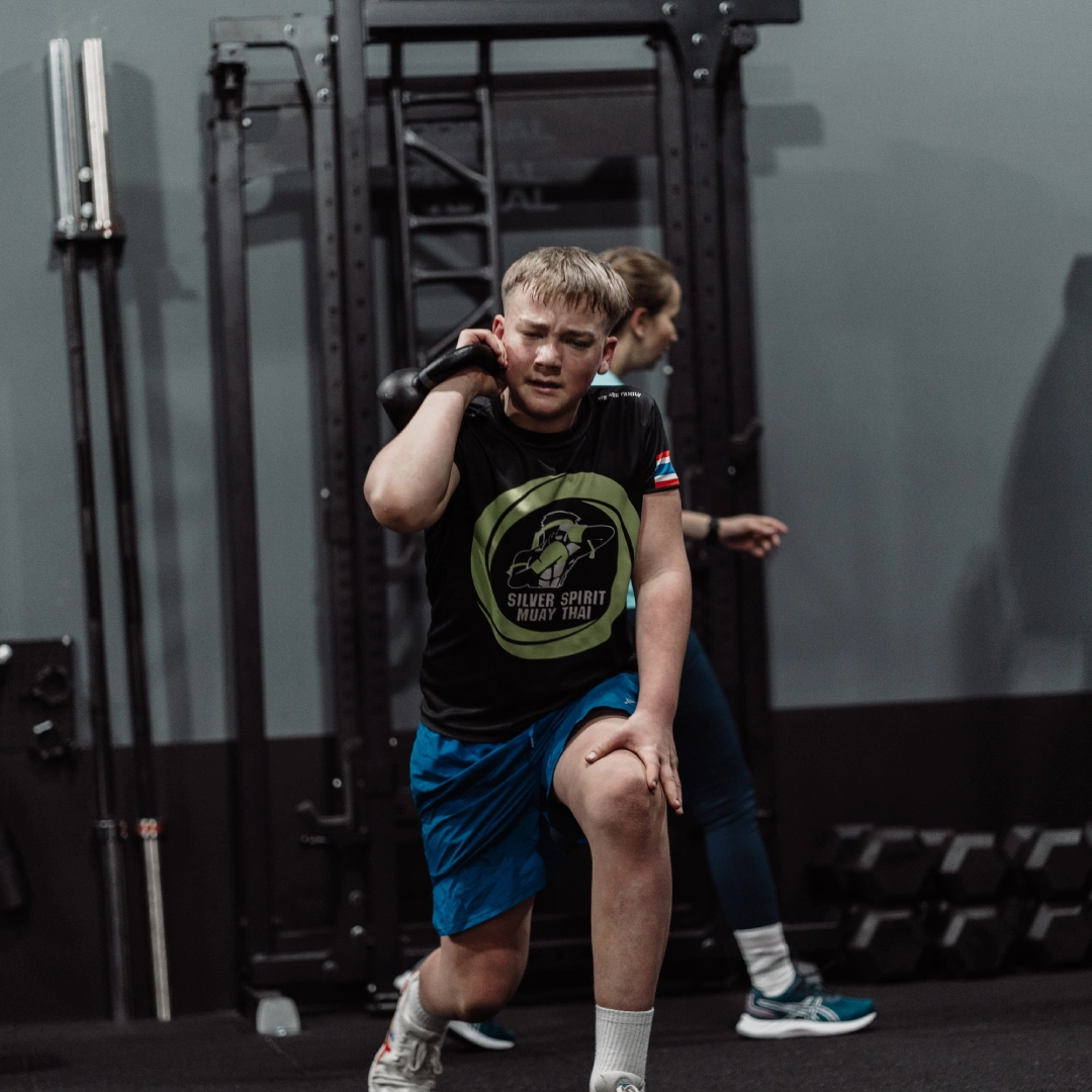 A young boy performs a squat in a gym at Unity Personal Training in Grays, ENG, focusing on his form and strength.