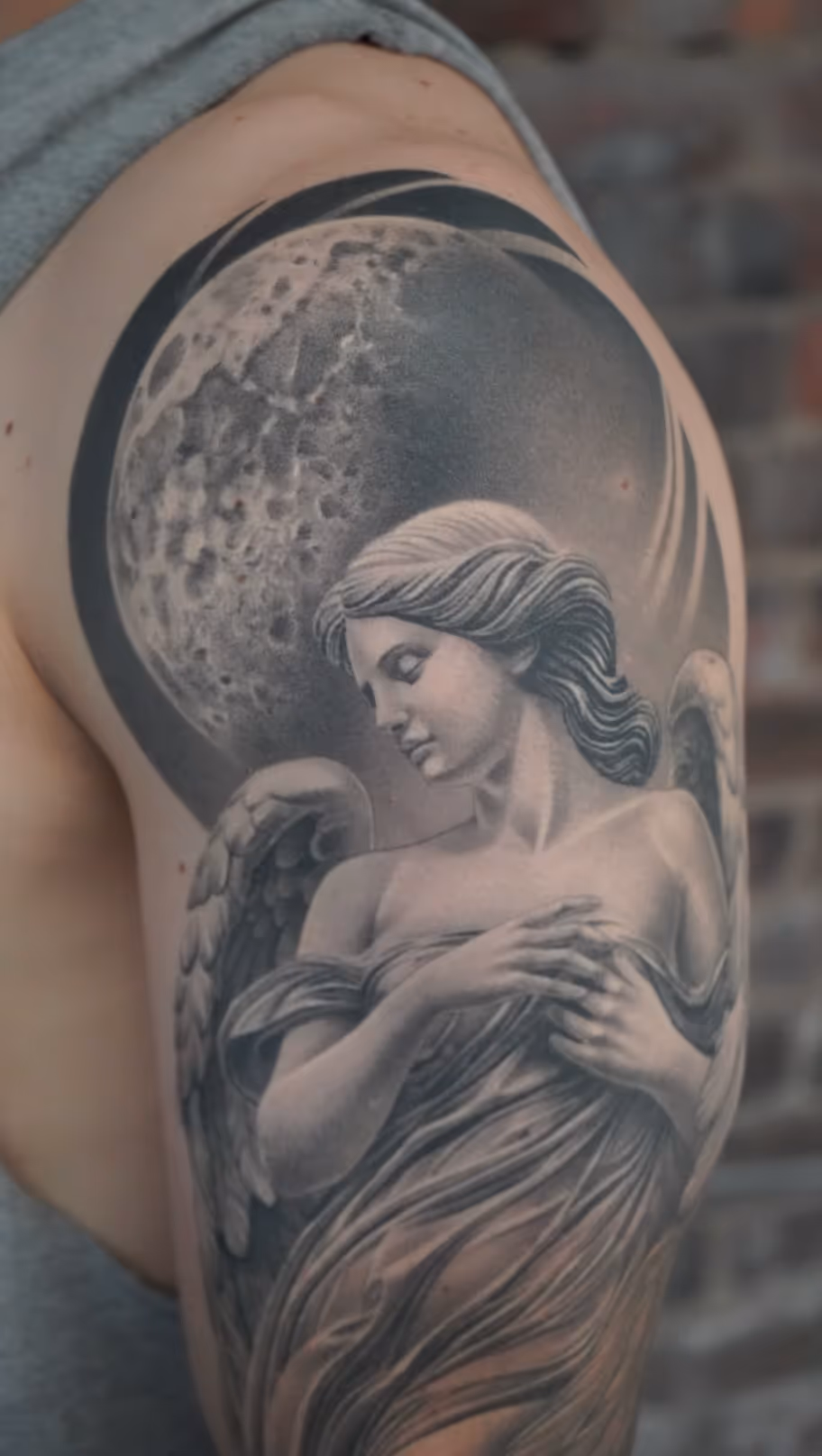 Black and grey realistic angel with wings and moon tattoo on upper arm
