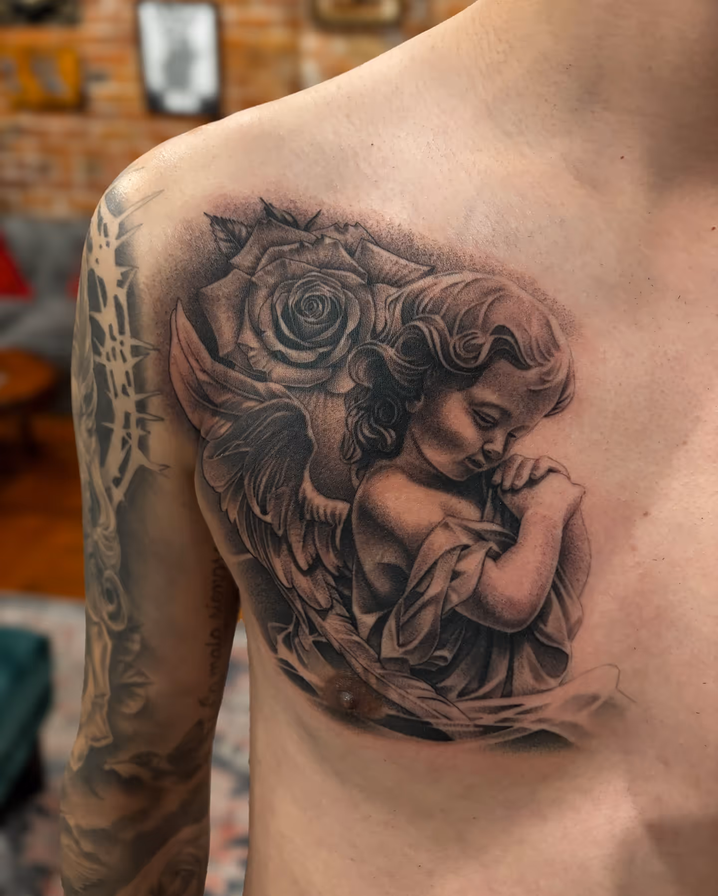 Black and gray chest tattoo of a praying cherub with a rose and wings