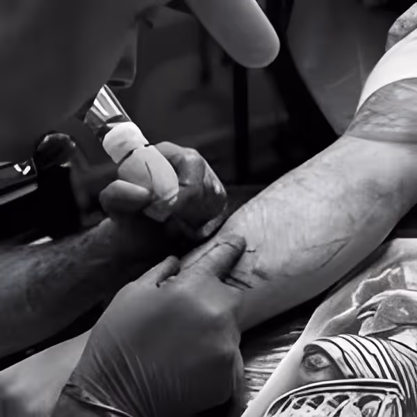 Tattoo artist in gloves using a machine to ink a forearm tattoo