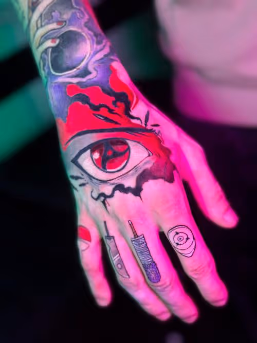 Hand with a bold red eye tattoo and small finger tattoos, lit by neon pink and green light